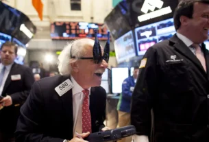 New York Stock Exchange Trader wearing champagne bottle-shaped glasses, smiling on trading floor.