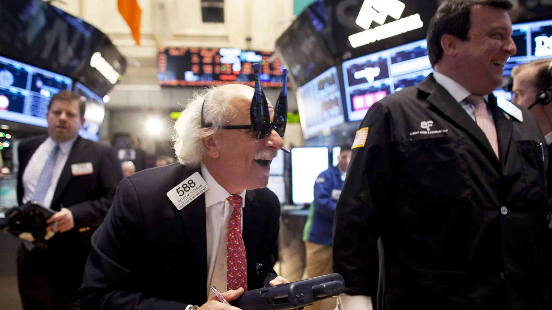 New York Stock Exchange Trader wearing champagne bottle-shaped glasses, smiling on trading floor.