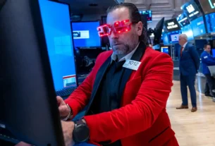 Stock trader wearing red jacket and "2025" shaped red glasses.